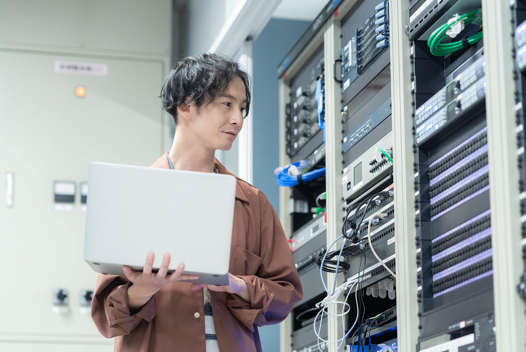 Engineer inspecting server infrastructure while managing cloud systems with laptop