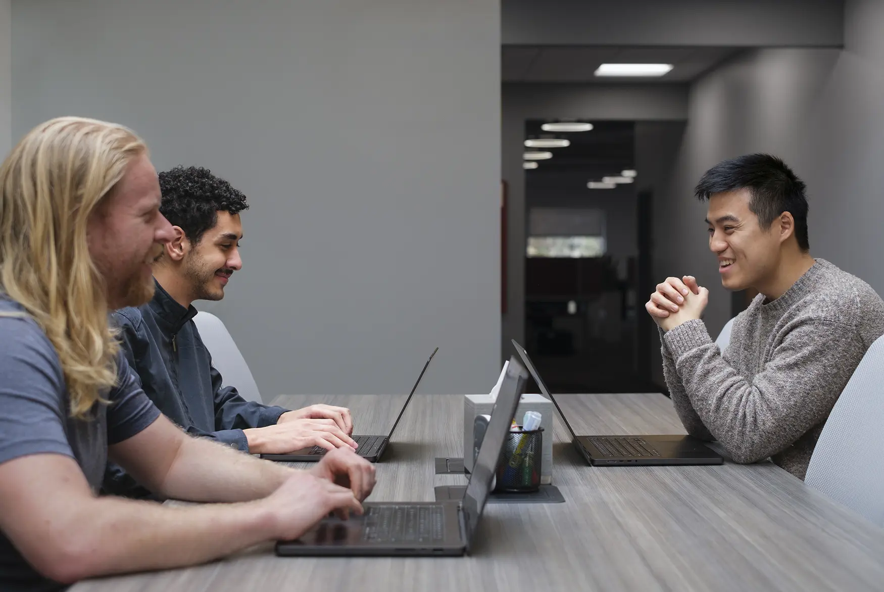 Employees discussing work across table while using laptops
